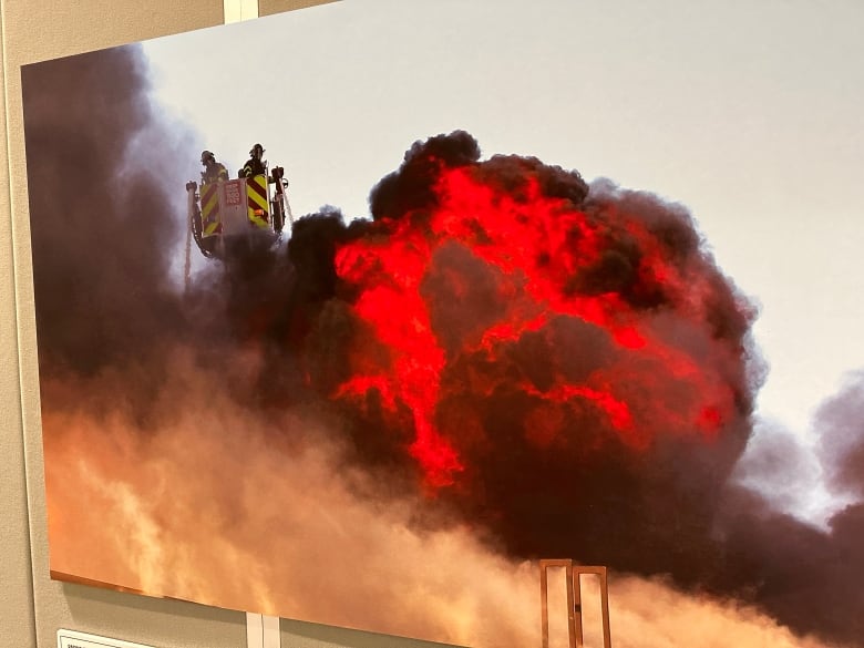 Photo of firefighters on a tower truck looking out at a ball of flames.